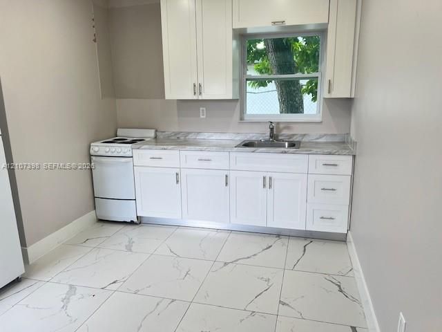 Kitchen featuring white shaker-style cabinetry, stone-pattern laminate countertops, stainless steel sink, large-format tile flooring with veining, and a freestanding electric range