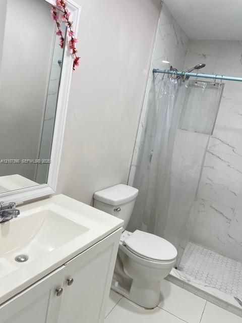 Bathroom featuring a vanity with an integrated countertop, wall-mounted mirror with white casing, walk-in shower with floor-to-ceiling stone-style tile surround, and hexagonal tile flooring