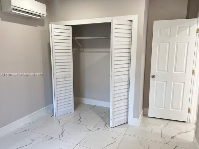 Large-format stone-look tile flooring, wall-mounted ductless climate control unit, white louvered-style bi-fold closet doors, and a solid-core interior door with satin nickel hardware