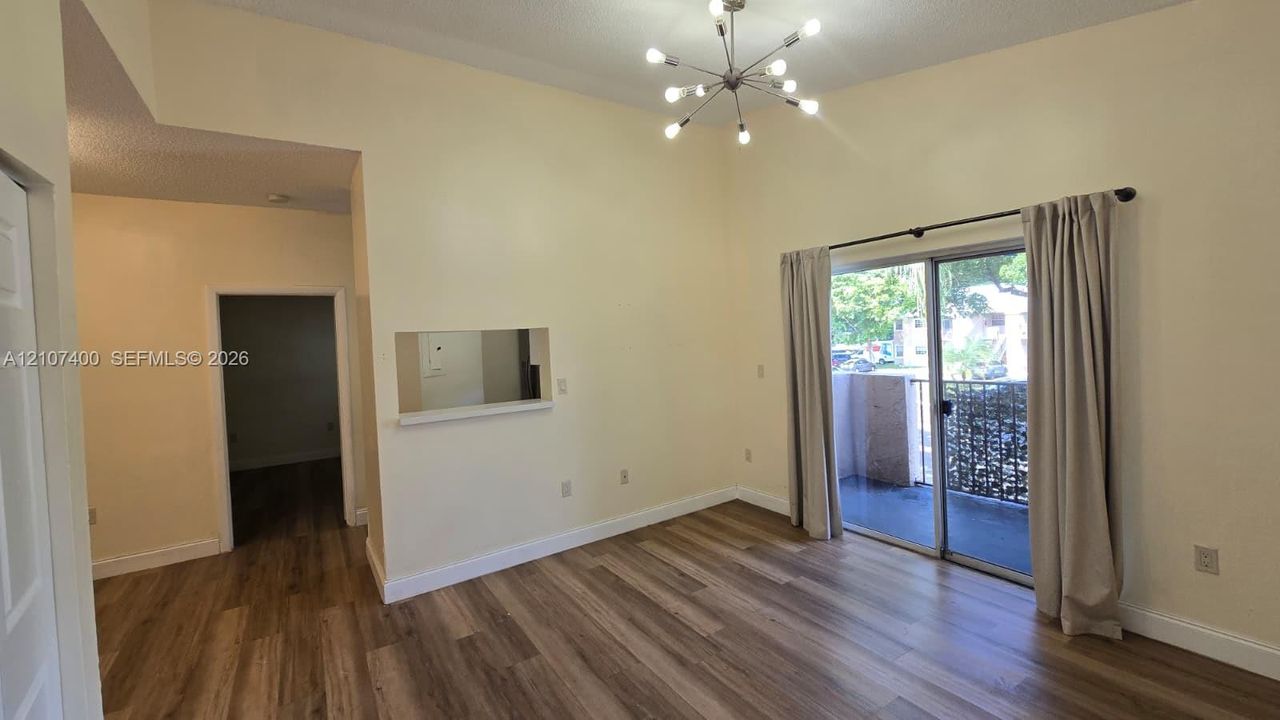 Living area featuring vaulted ceilings, wood-finish flooring, a multi-arm sputnik-style light fixture, pass-through wall opening, and sliding glass doors leading to a private balcony