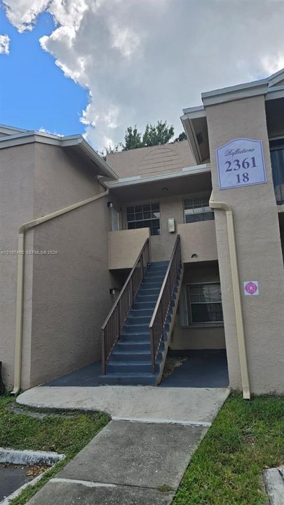 Stucco exterior building with an outdoor staircase, metal railings, and concrete sidewalk