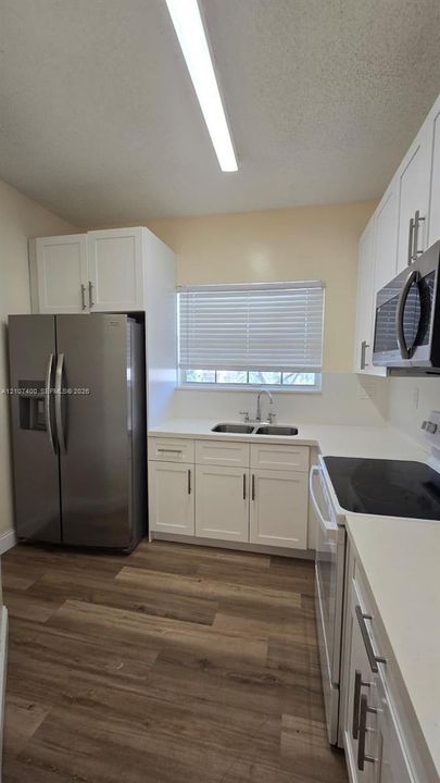 Kitchen featuring white cabinetry with stainless steel pulls, solid surface countertops, stainless steel side-by-side refrigerator, microwave, and wood-finish flooring