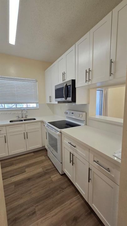 Kitchen featuring shaker-style white cabinetry, solid-surface countertops, wood-finish flooring, integrated microwave, and double-basin stainless steel sink