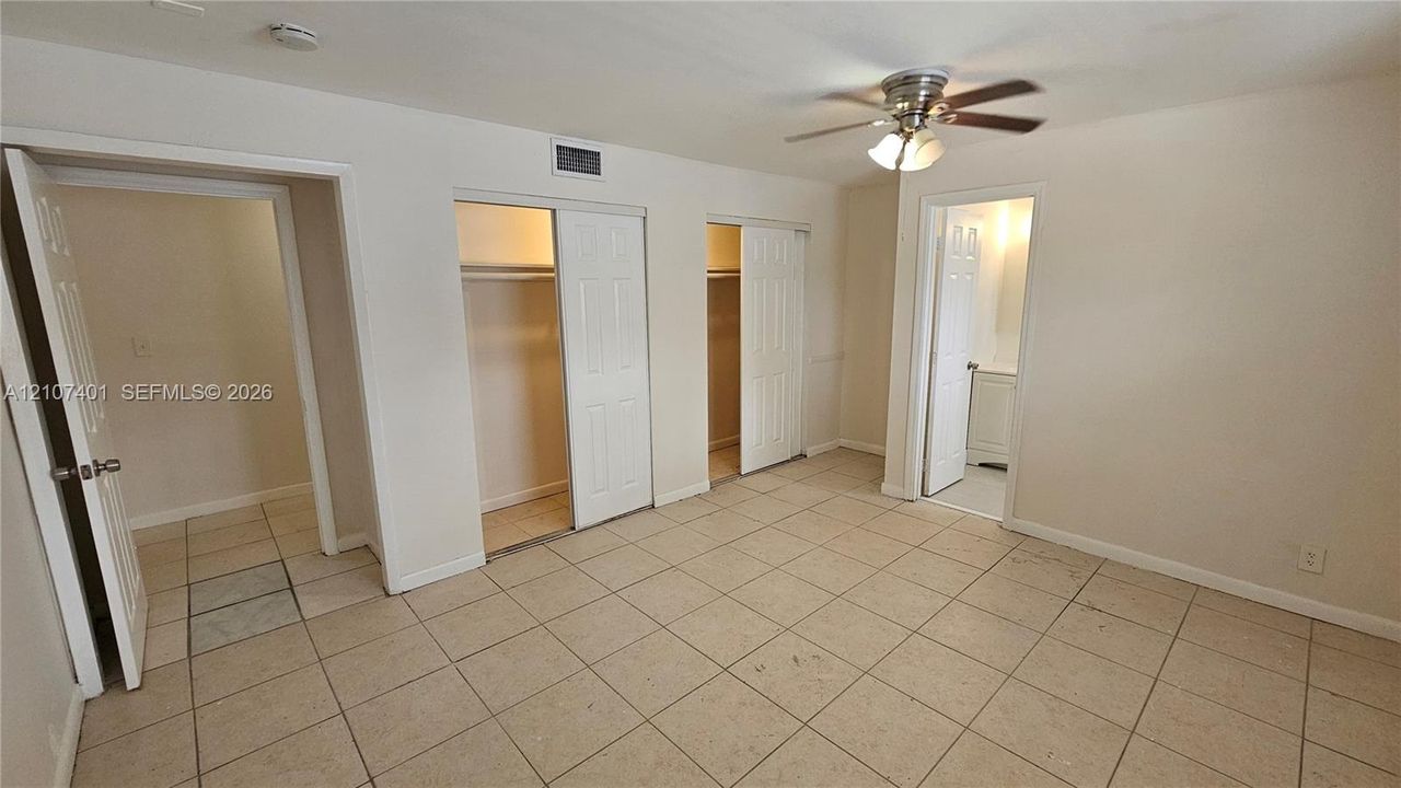 Tile flooring, ceiling fan with integrated lighting, and dual reach-in closets featuring multi-panel doors