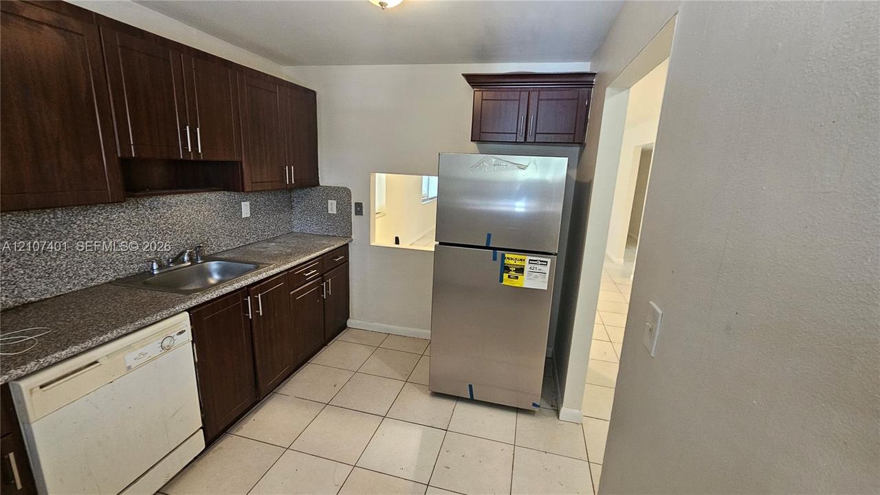 Kitchen featuring dark-stained wooden cabinetry, stone-finish countertops, stainless steel refrigerator, and tiled flooring