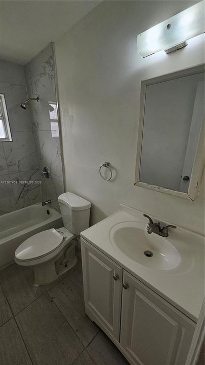 Bathroom featuring a vanity with a drop-in sink, wall-mounted vanity lighting, a bathtub and shower combination with large-format tile surround, and tile flooring