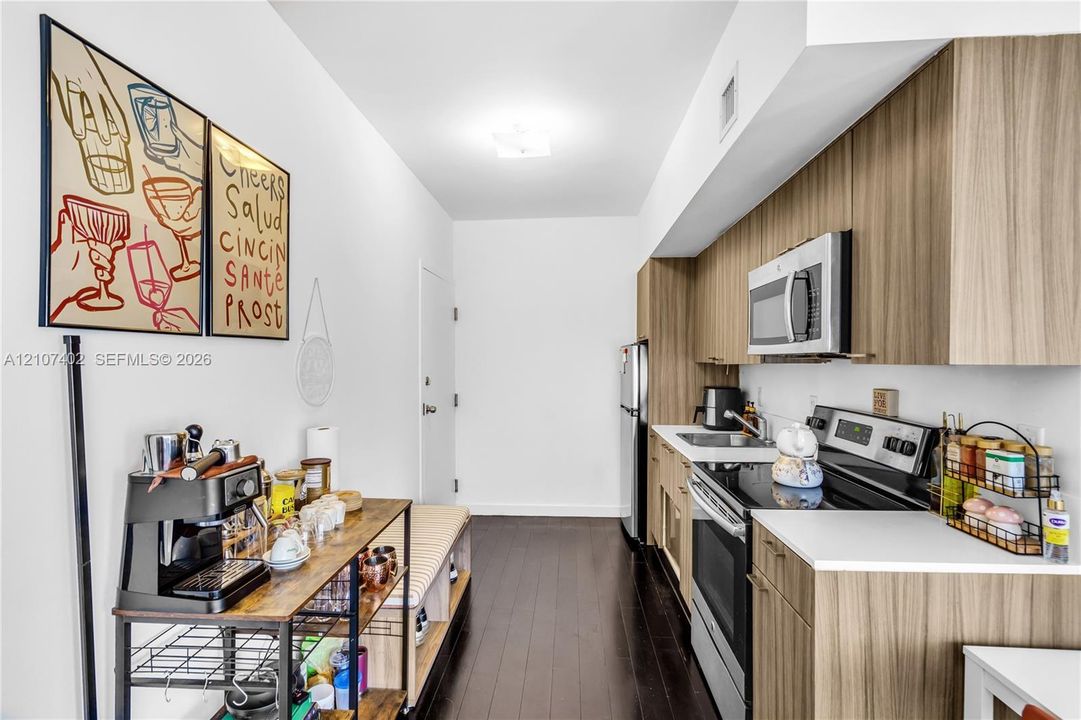 Kitchen featuring horizontal grain wood-finish cabinetry, white countertops, stainless steel appliances, and dark wood-finish flooring