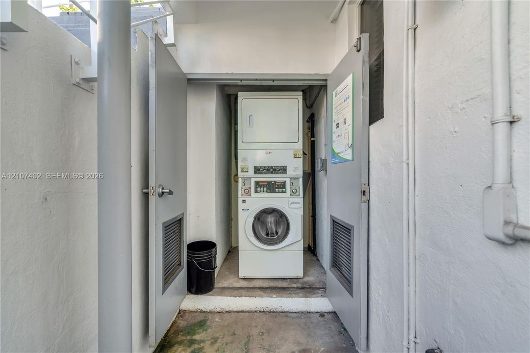 Laundry alcove featuring a stacked washer and dryer unit enclosed by louvered-panel dual doors