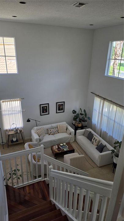 High-ceiling living area featuring multi-level windows, wood-finish staircase treads, and white vertical baluster railing