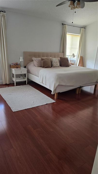 Bedroom featuring wood-finish flooring, a ceiling fan with integrated lighting, and window treatments