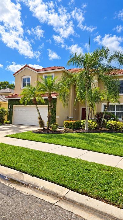 Two-story residence featuring a terracotta-tiled roof, stucco exterior, multi-pane windows, and a paved driveway leading to an attached two-car garage