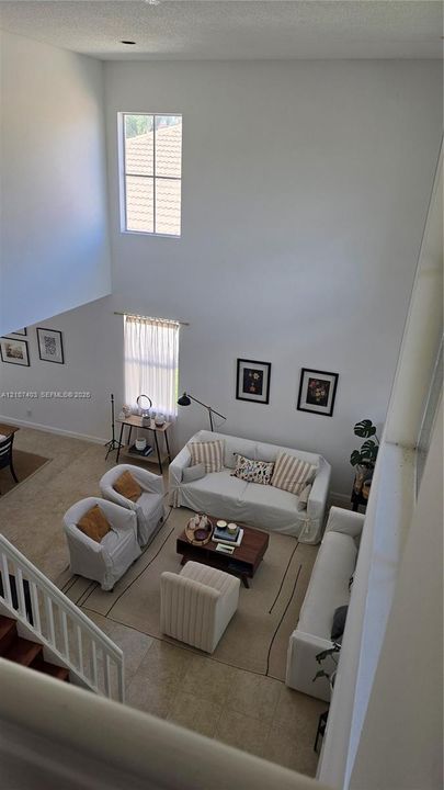 High-ceiling interior featuring multi-level windows, neutral tile flooring, and white spindle staircase railing