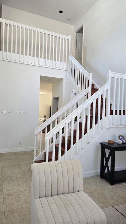 High-ceiling foyer featuring a staircase with wood-finish treads, white railings, and tile flooring