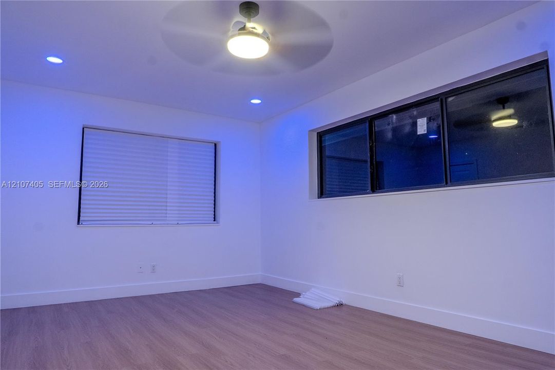 Interior space featuring wood-finish flooring, recessed lighting, a ceiling fan with integrated light, a paneled interior door, and large windows with dark frames