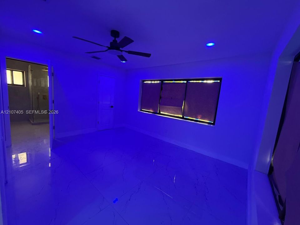 Large-format tile flooring, mirrored feature wall with built-in electric fireplace, recessed lighting, sculptural pendant light fixture, and kitchen island with waterfall-edge countertop
