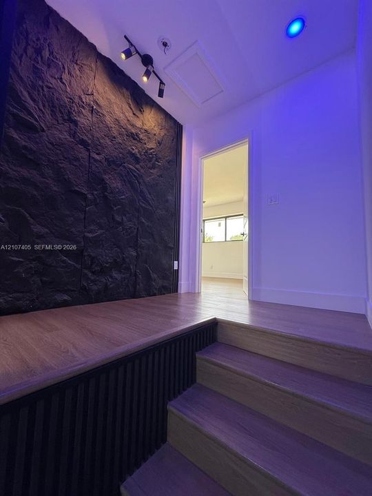 Neutral-toned room featuring dark wood-finish flooring, three black-framed windows, a ceiling fan with integrated lighting, and a wall-mounted ductless air conditioning unit