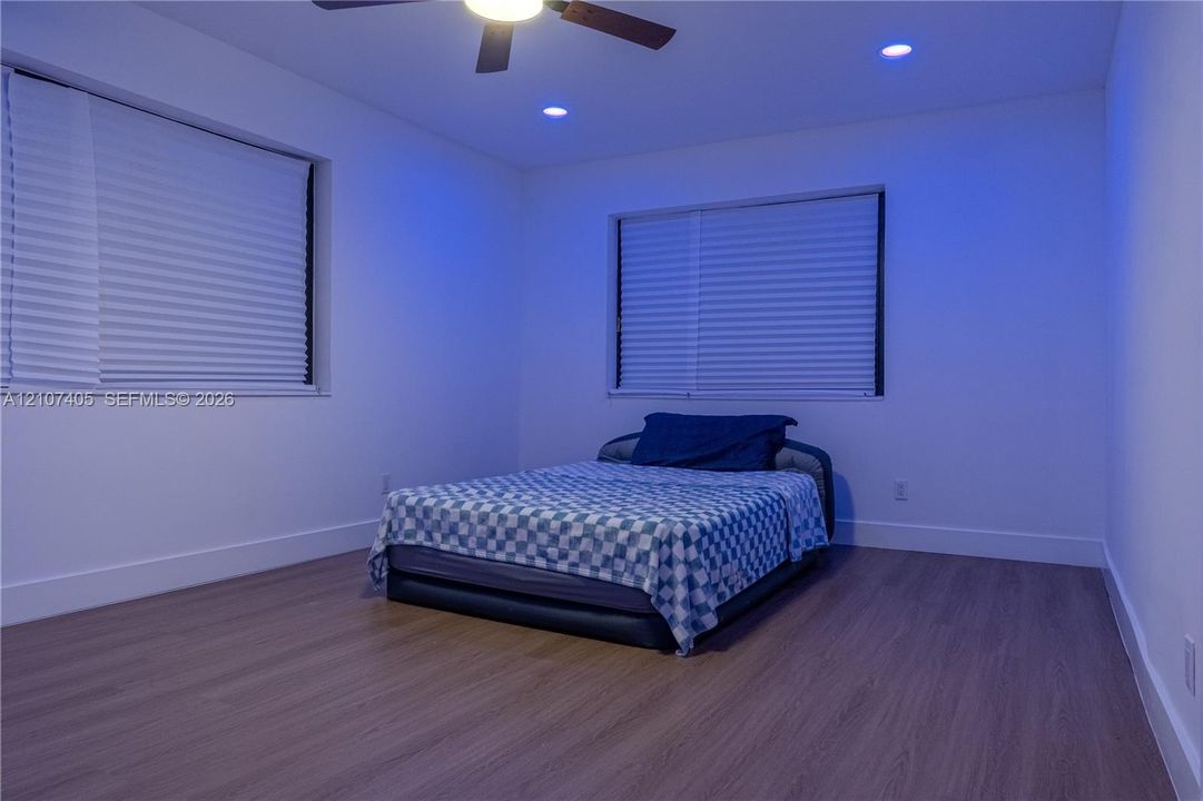 Wood-finish flooring, recessed lighting, ceiling fan with integrated light, pleated window shade, and solid-core interior door with matte black hardware