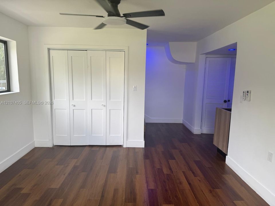 Neutral interior room featuring wood-finish flooring, recessed lighting, a ceiling fan with dark finish blades, and large windows with black frames