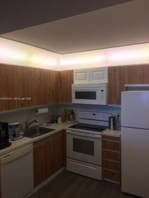 Kitchen featuring wood-finish cabinetry, white appliances, integrated cove lighting, and chevron-patterned tile backsplash