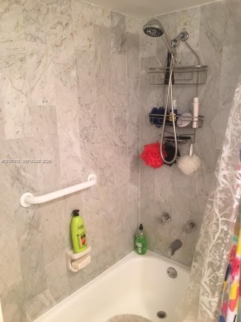 Shower enclosure featuring stone-tiled walls, a built-in soap dish, a wall-mounted grab bar, and a chrome-finish shower fixture