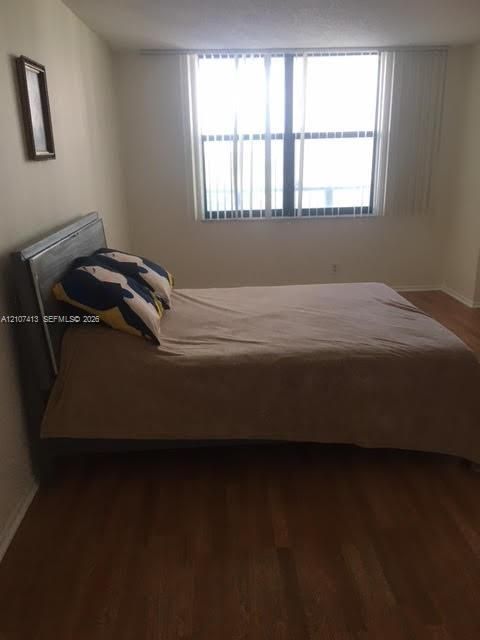 Room featuring wood-finish flooring and a large window with vertical blinds