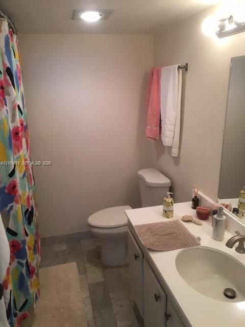 Bathroom featuring a single-basin vanity with a solid-surface countertop, an undermount sink, multi-tone tile flooring, and a wall-mounted light fixture