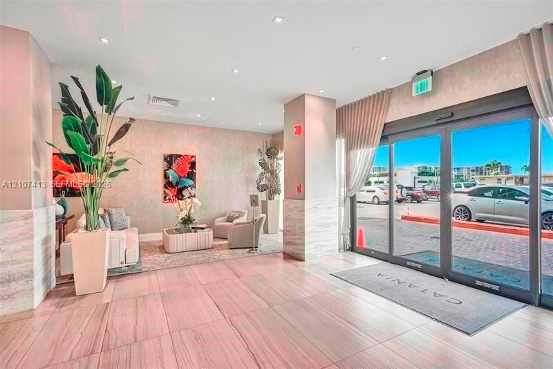 Lobby entrance featuring large-format tile flooring, stone-accented columns, floor-to-ceiling glass sliding doors, and recessed ceiling lighting