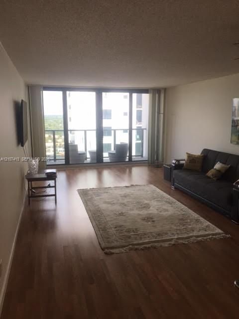 Living area featuring wood-finish flooring, floor-to-ceiling windows, and a glass-paneled balcony