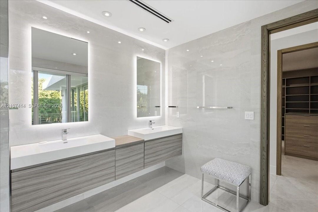 Floating double vanity with wood-finish cabinetry, integrated rectangular sinks, polished chrome fixtures, back-lit vanity mirrors, and floor-to-ceiling large-format tile wall cladding