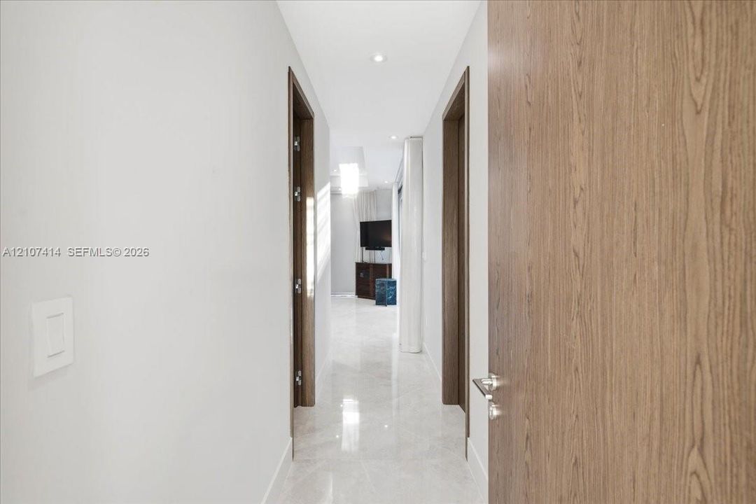 Hallway featuring large-format light-toned stone flooring, recessed ceiling lighting, and solid wood-finish doors with brushed-metal hardware