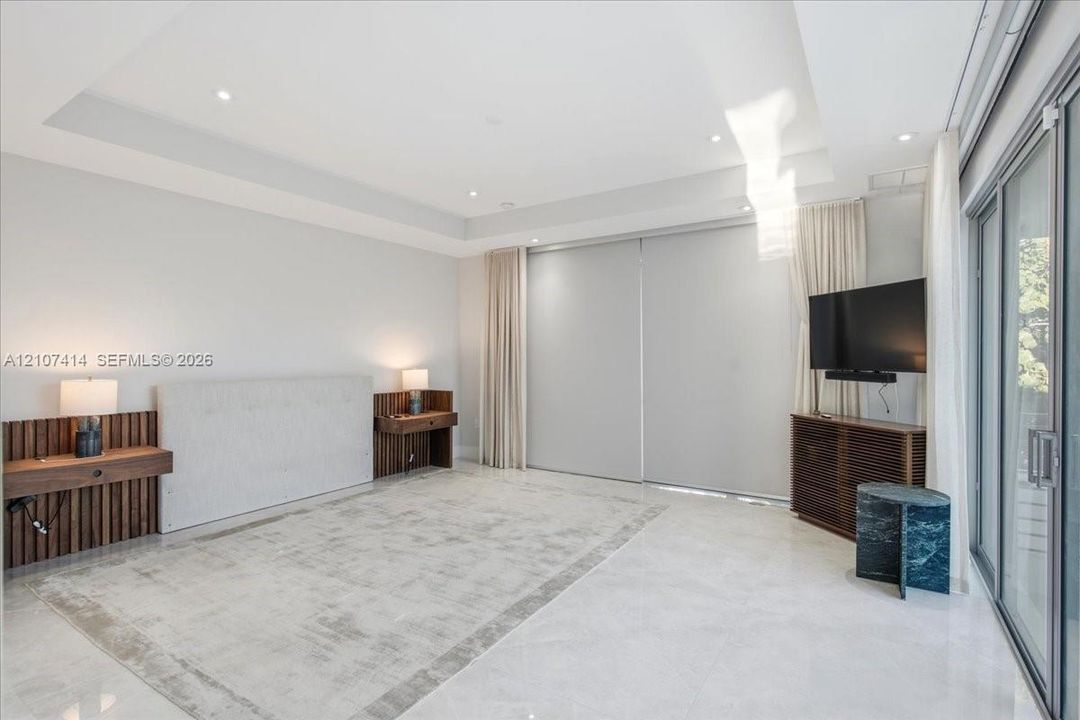 Tray ceiling with recessed lighting, integrated wood-slat wall paneling, built-in wooden shelving, oversized tile flooring, and floor-to-ceiling sliding glass doors