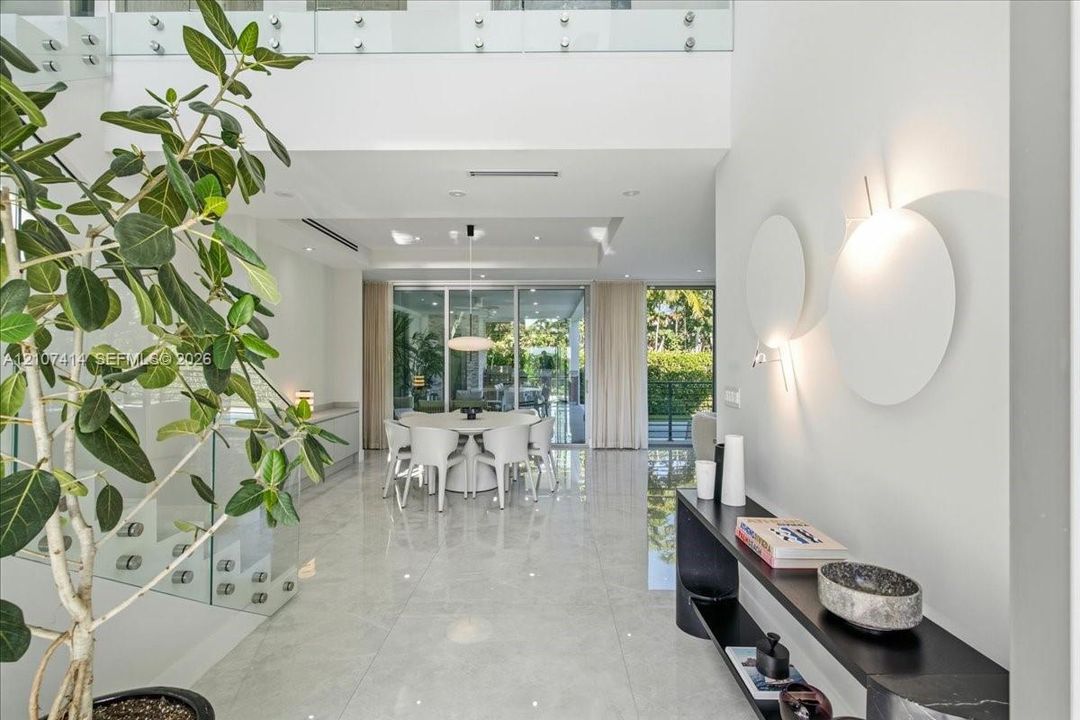 Double-height entryway featuring polished tile flooring, glass-panel staircase railing, recessed lighting, and wall-mounted circular accent fixtures