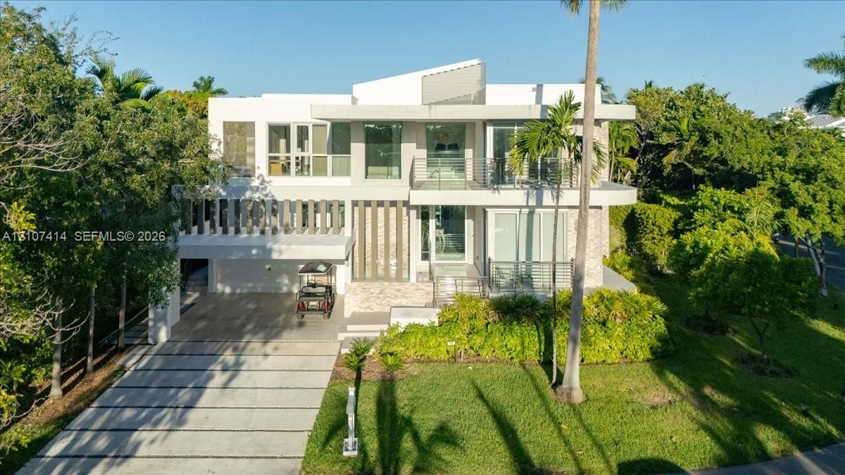 Contemporary two-story architectural exterior featuring clean lines, a multi-level balcony with metal railings, stone cladding, and a paved driveway with integrated linear drainage