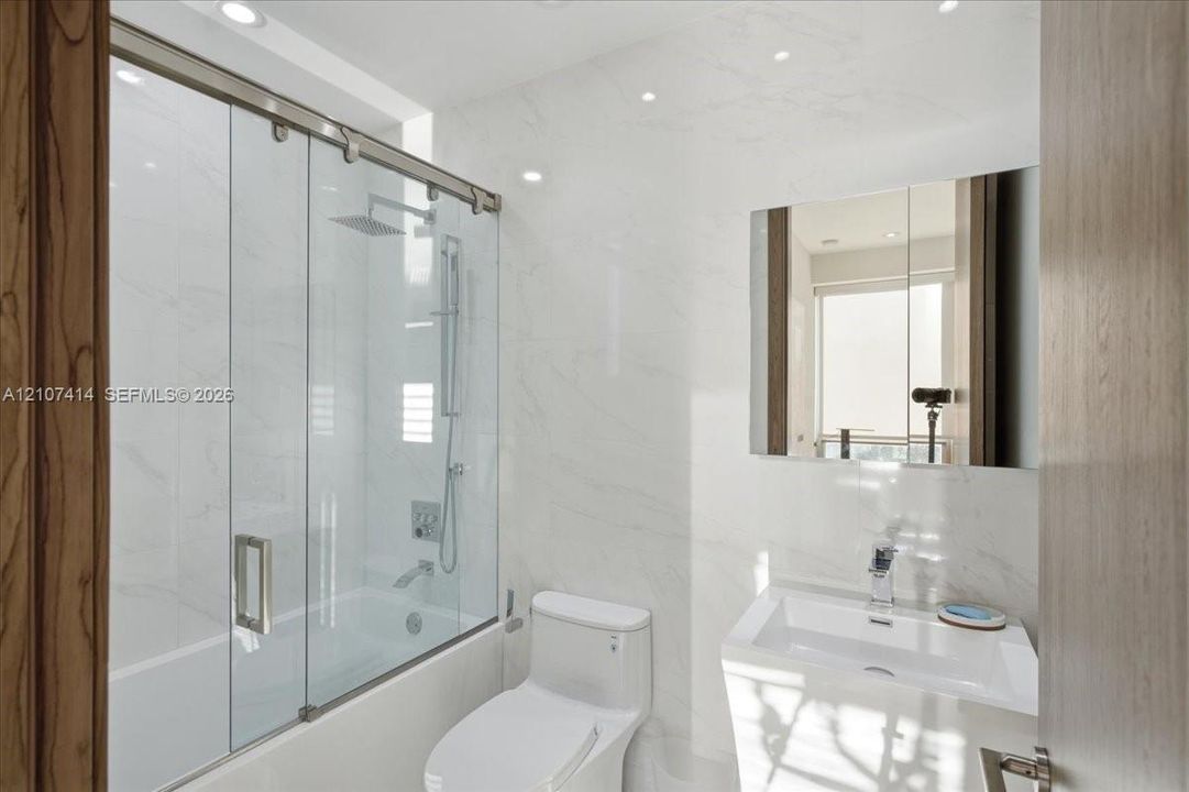 Bathroom featuring full-height stone-finish wall tile, a glass-enclosed shower with a rainfall showerhead, a wall-mounted medicine cabinet, and a contemporary pedestal sink with a chrome faucet