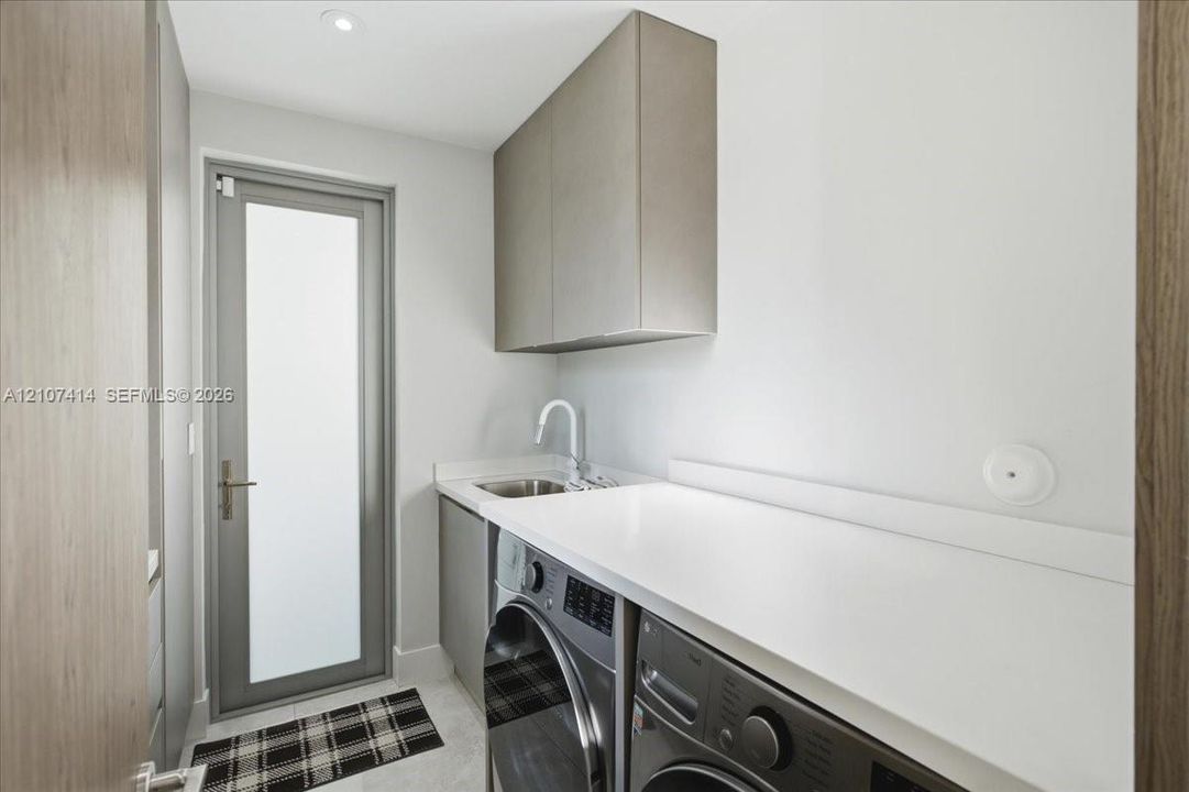 Utility room featuring custom cabinetry, a solid surface countertop, an undermount sink with a high-arch faucet, and a glass-panel door