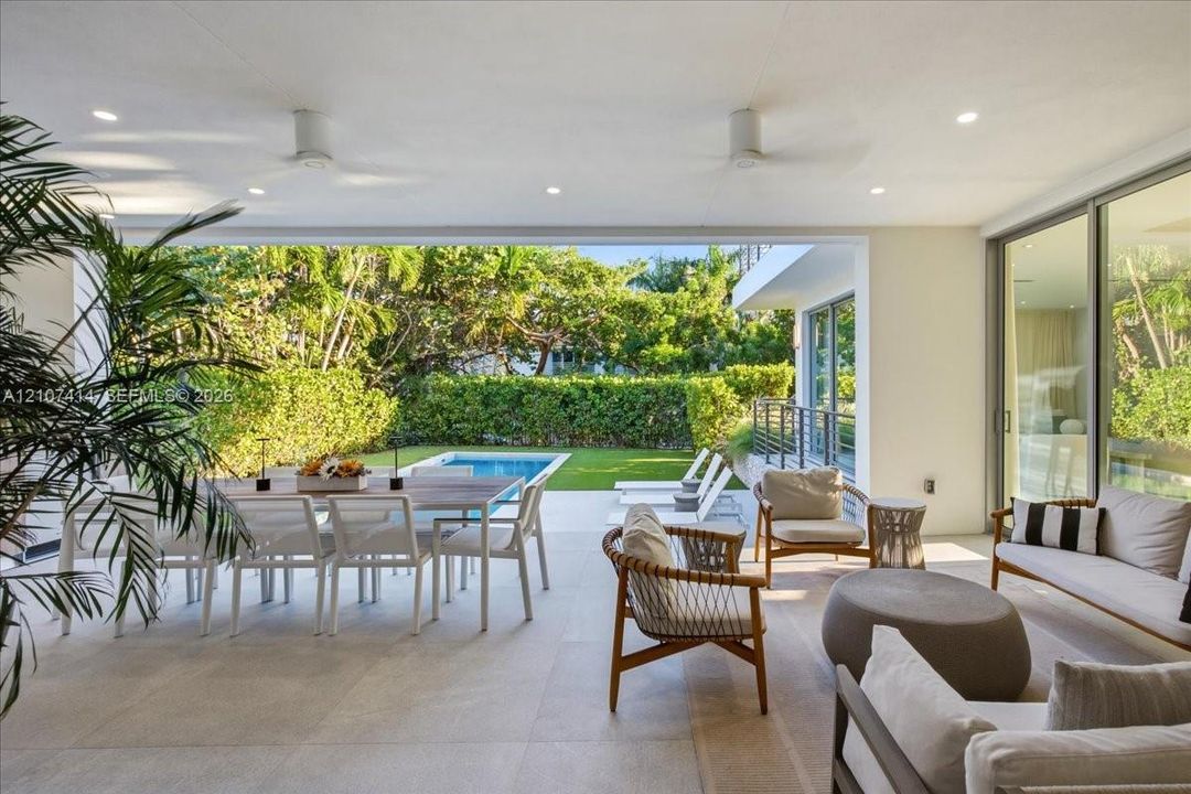 Covered patio featuring large-format stone-finish flooring, recessed lighting, ceiling fans, floor-to-ceiling glass sliding doors, and direct access to an outdoor swimming pool and manicured lawn