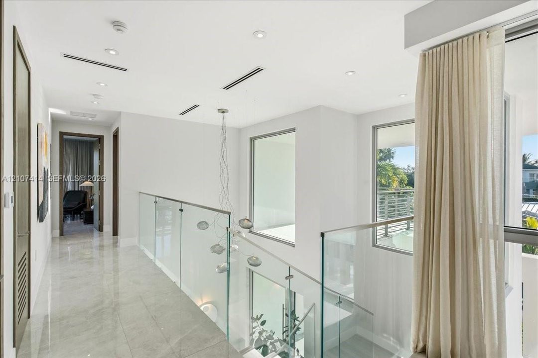 Hallway featuring polished stone flooring, glass panel railing, recessed ceiling lighting, and floor-to-ceiling windows