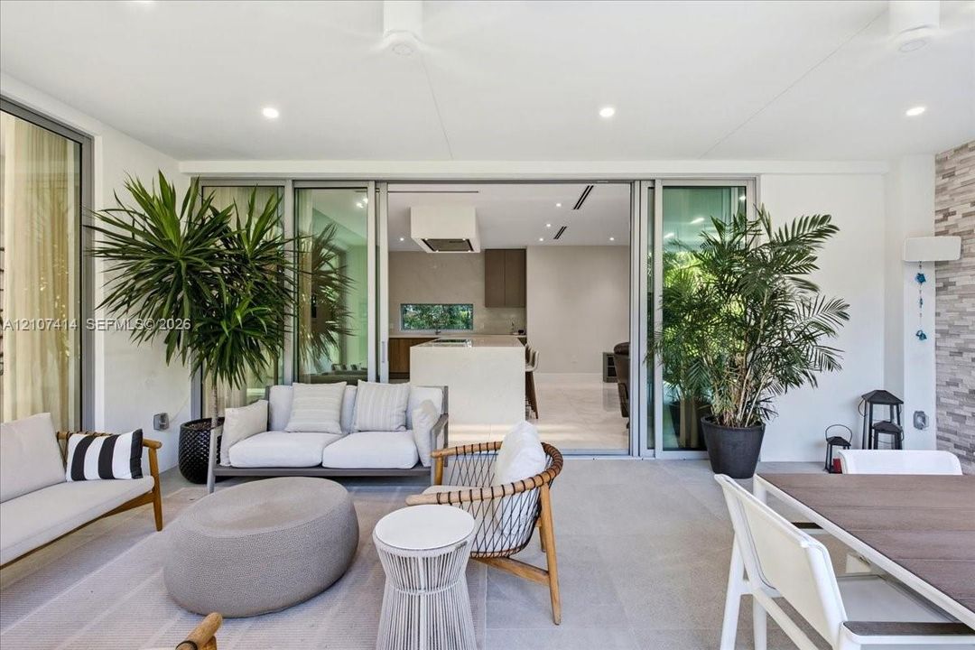 Covered patio featuring large-format stone-finish flooring, recessed ceiling lighting, and expansive floor-to-ceiling multi-panel sliding glass doors with thin-profile frames