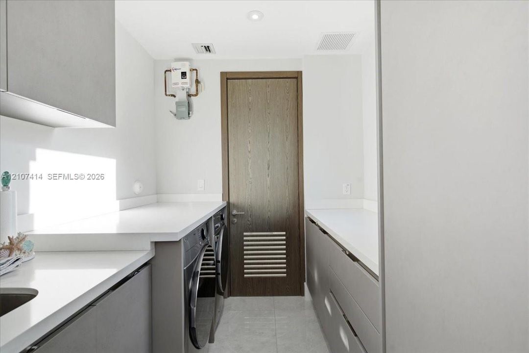 Laundry room featuring grey flat-panel cabinetry, white solid-surface countertops, integrated sink, and wood-finish door with louvered panel
