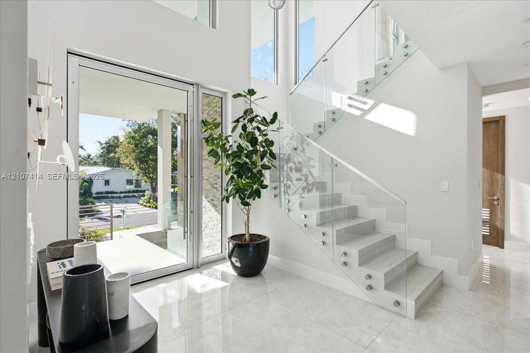 Entryway featuring polished stone flooring, a multi-story ceiling, floor-to-ceiling windows, and a floating staircase with glass panel railings