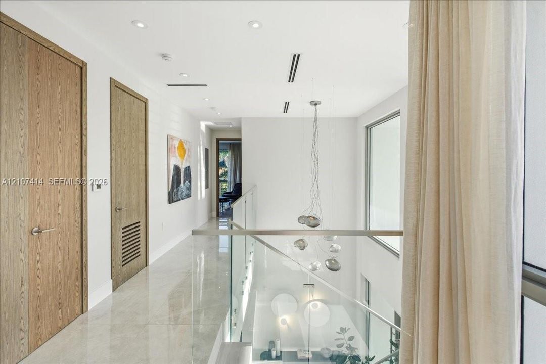 Hallway featuring large-format light tile flooring, wood-finish interior doors, recessed lighting, and a glass panel railing