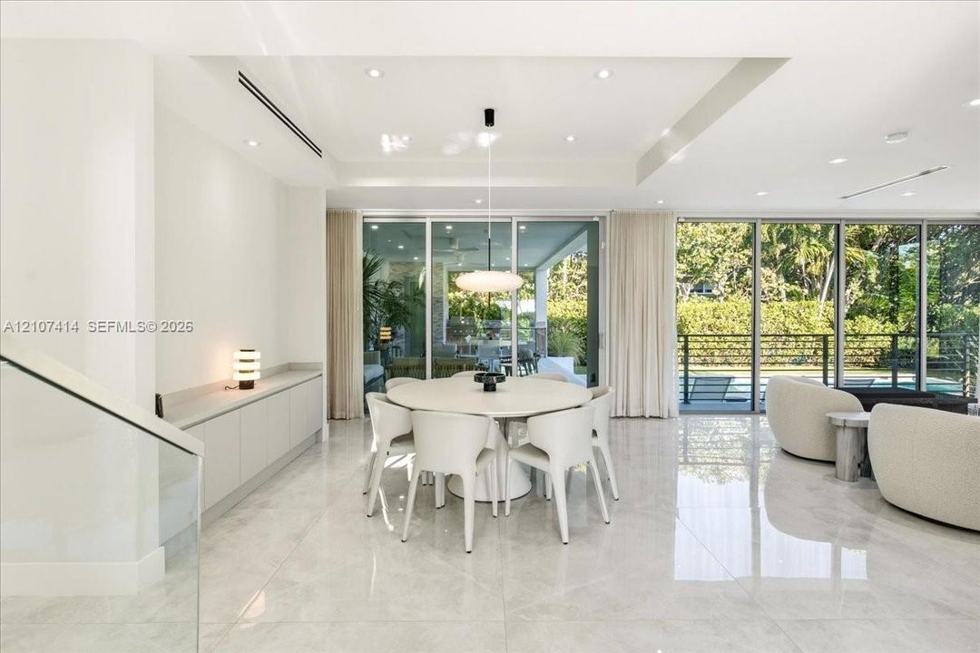 Open-concept interior featuring large-format tile flooring, floor-to-ceiling glass sliding doors, recessed lighting, and custom built-in cabinetry with a stone-top surface