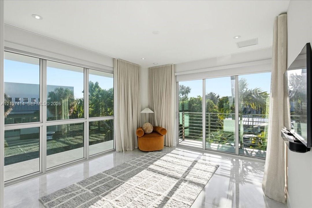 Floor-to-ceiling glass windows, recessed ceiling lighting, light-toned tile flooring, and a private balcony with metal railing