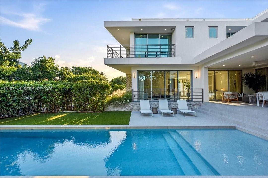 Modern exterior featuring a swimming pool, concrete patio, glass sliding doors, stone masonry accents, and a second-story metal railing balcony