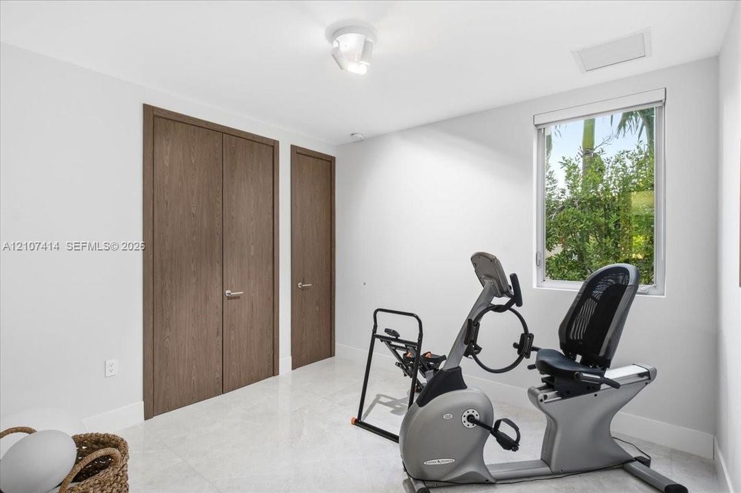 Neutral-toned interior space featuring light-colored stone-finish flooring, solid wood-finish doors with metallic hardware, and a single-pane window with a view of greenery