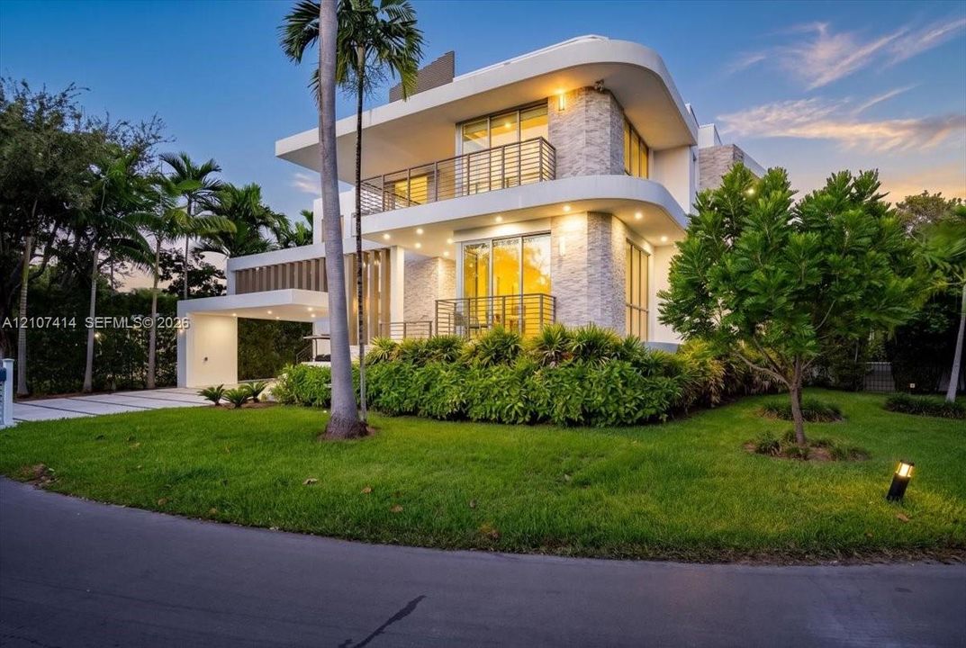 Modern multi-level exterior featuring curved architectural lines, stone-clad facade, metal balcony railings, and a covered porte-cochère