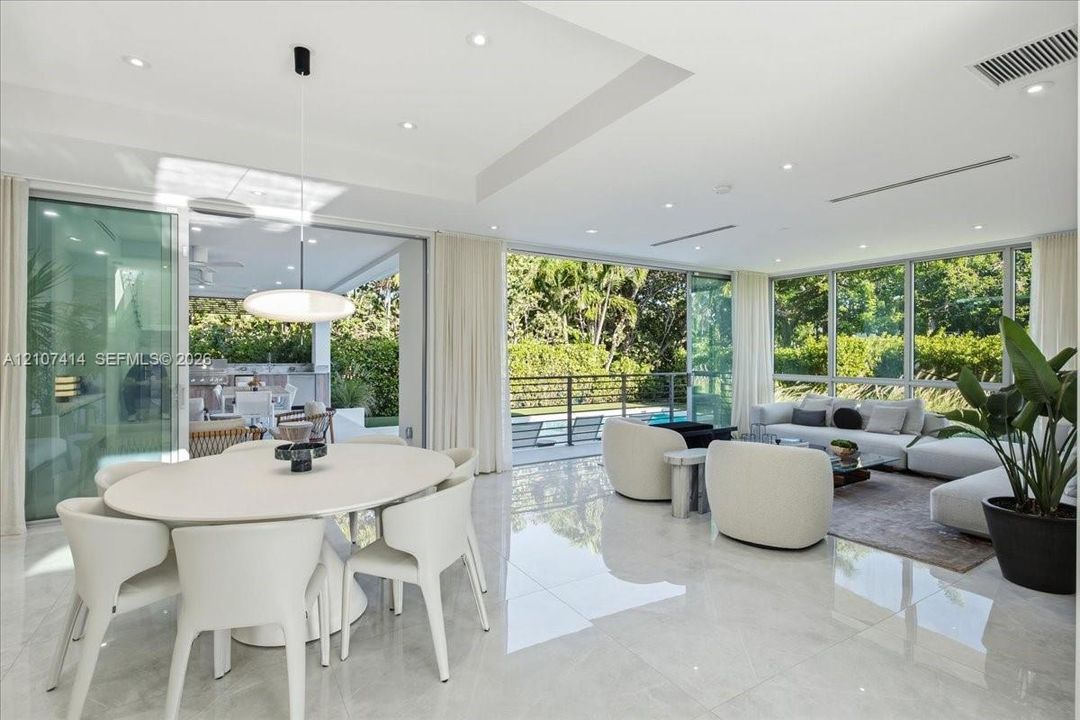 Open-concept living space featuring floor-to-ceiling glass sliding doors, polished tile flooring, recessed ceiling lighting, and a tray ceiling design