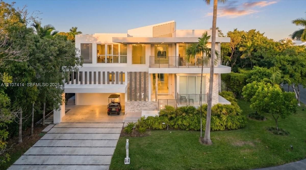 Modern multi-level exterior featuring white stucco finishes, natural stone accents, glass balcony railings, and a covered ground-level parking area with a concrete paver driveway