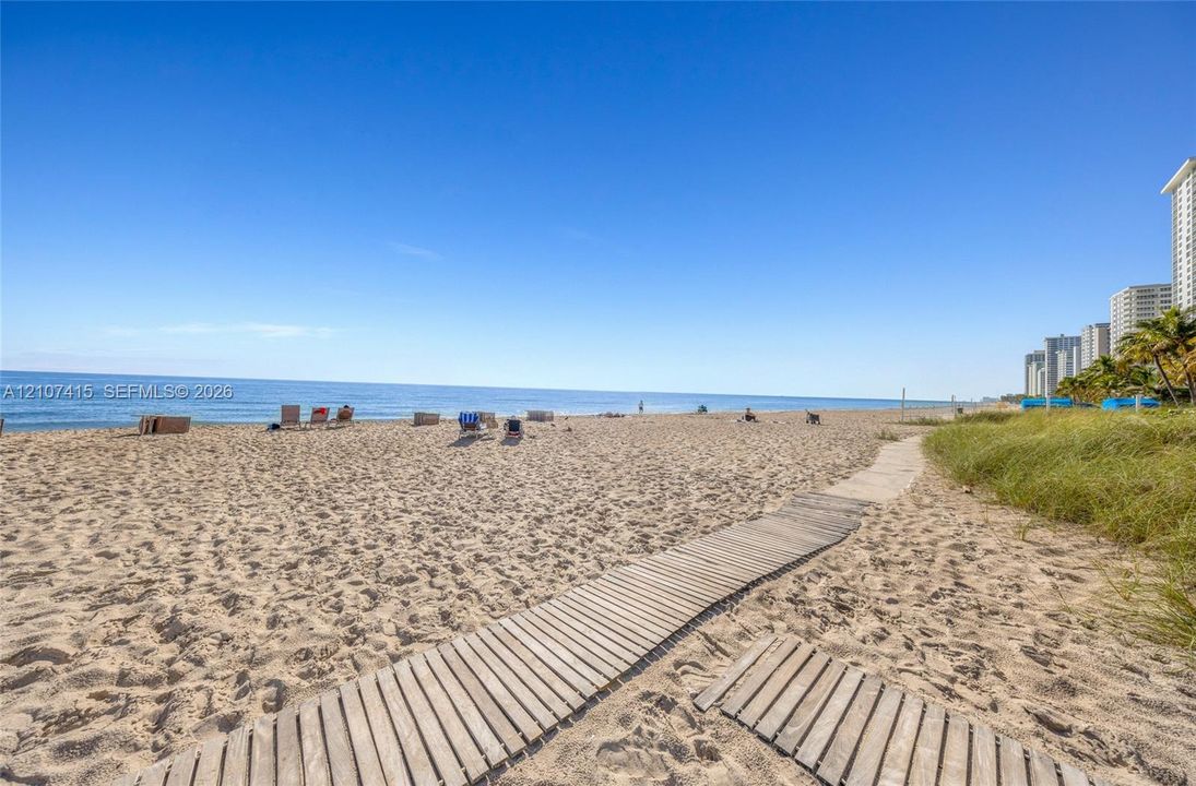 Sandy beach frontage with direct ocean access, natural sand dunes, and a wood-slat walkway