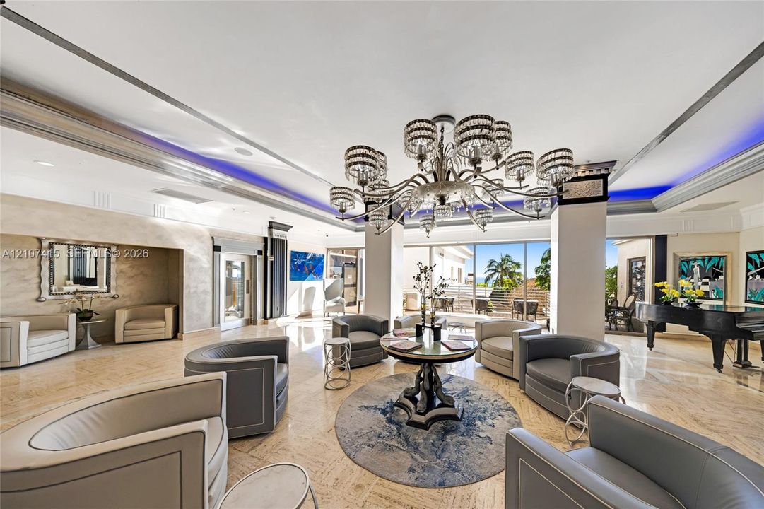 Expansive living area featuring polished stone flooring, recessed ceiling lighting with perimeter accent illumination, a tiered crystal chandelier, and floor-to-ceiling glass sliding doors